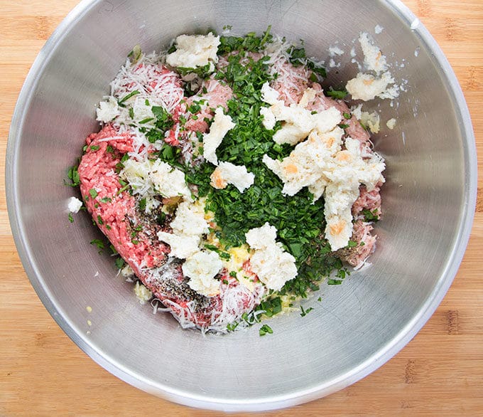 stainless steel bowl filled the ingredients to make Italian meatballs