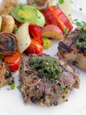 grilled lamb chops with a mint pesto on a white plate with grilled vegetables