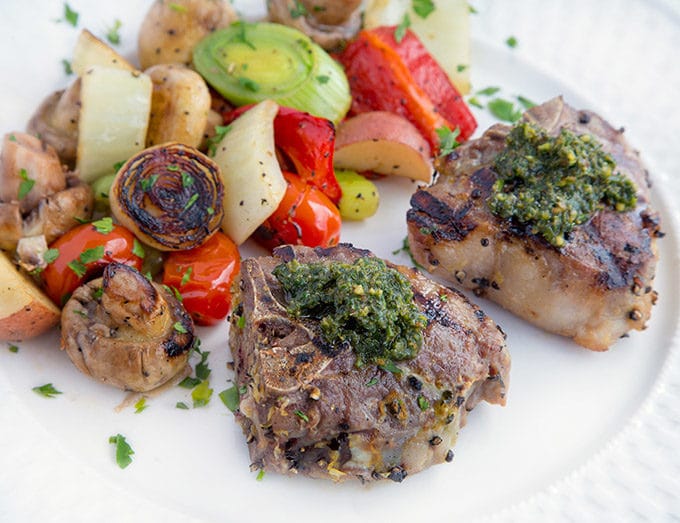 grilled lamb chops with a mint pesto on a white plate with grilled vegetables