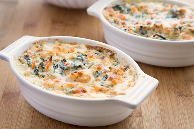 two white oval baking dishes filled with salmon dip on a wooden cutting board