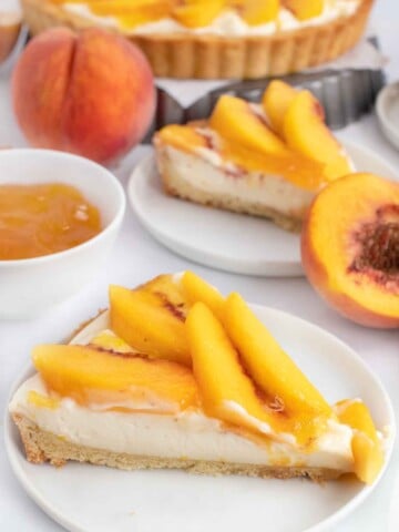 two slices of peach tart on white plates with whole tart behind them