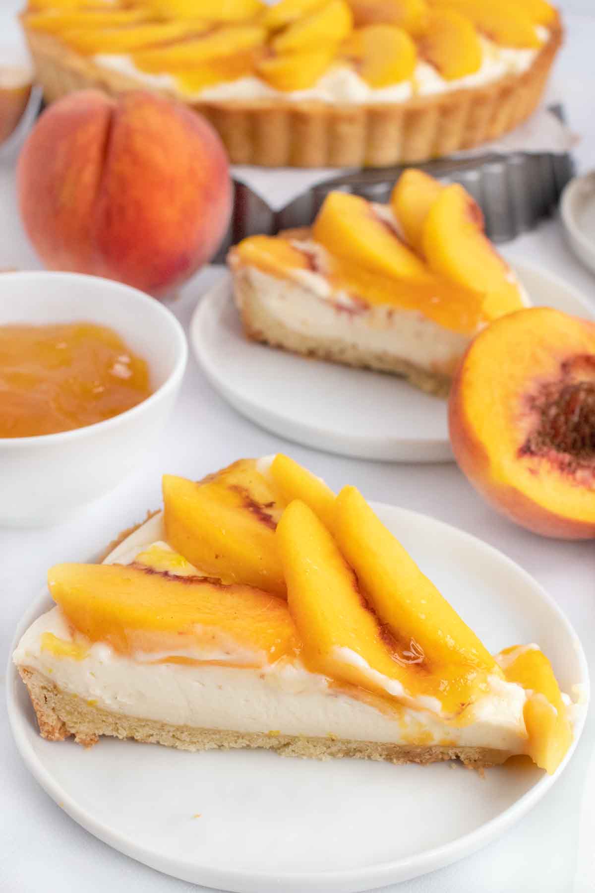 two slices of peach tart on white plates with whole tart behind them