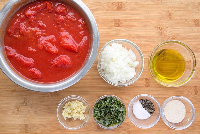 ingredients to make tomato sauce in glass bowls sitting on a wooden cutting board