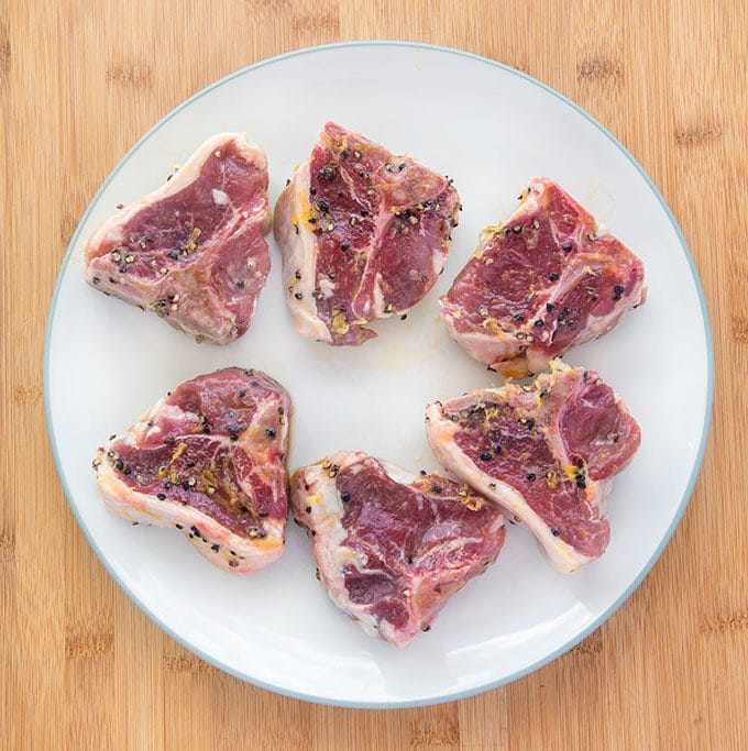 marinated lamb chops on a white plate on top of a wooden cutting board