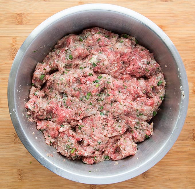 Italian meatball mixture sitting in a stainless steel bowl on top of a wooden cutting board