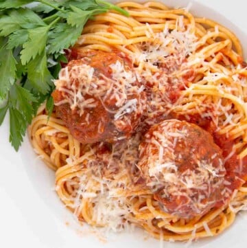spaghetti and meatballs with a sprig of Italian parsley on a white bowl