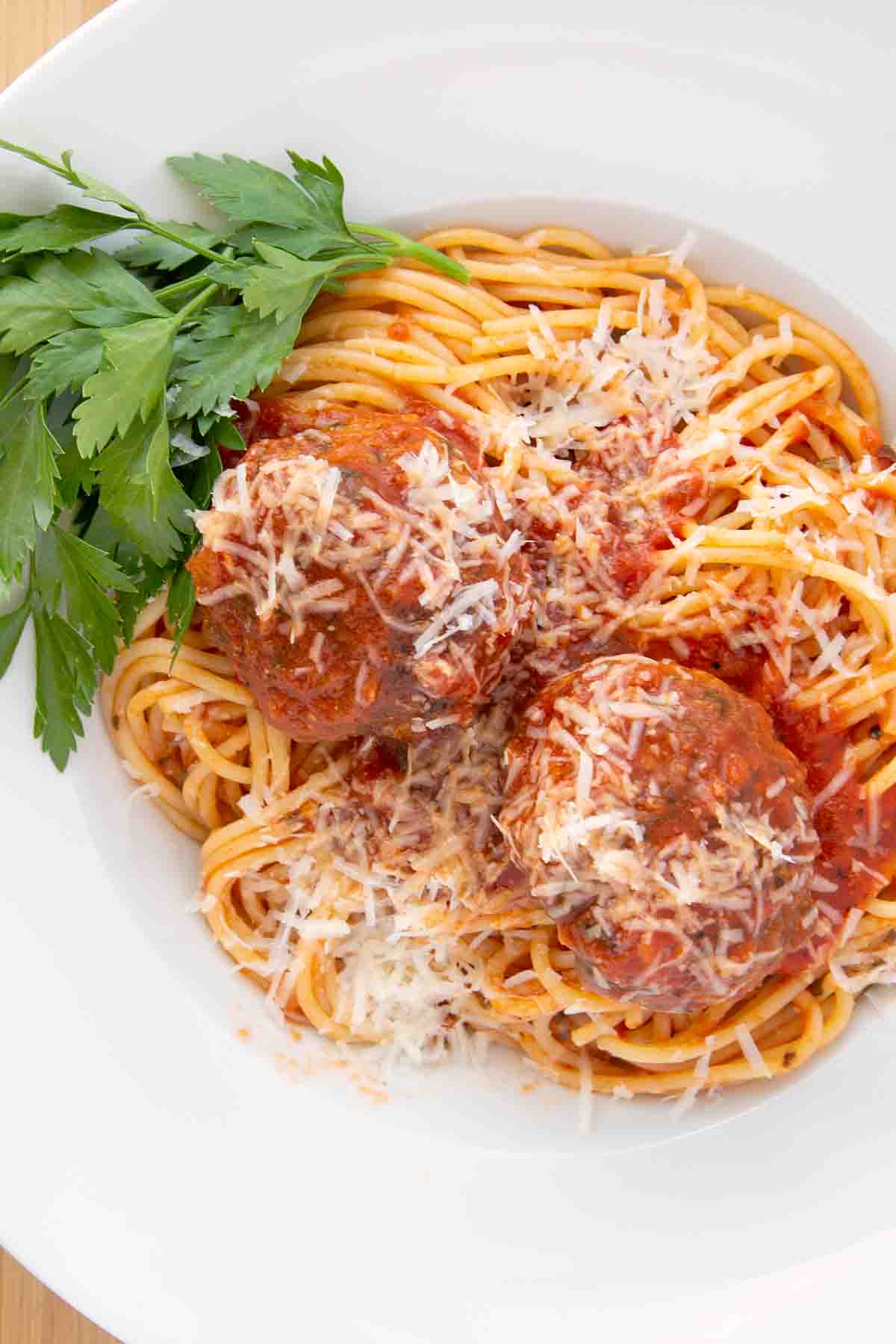 spaghetti and meatballs with a sprig of Italian parsley on a white bowl