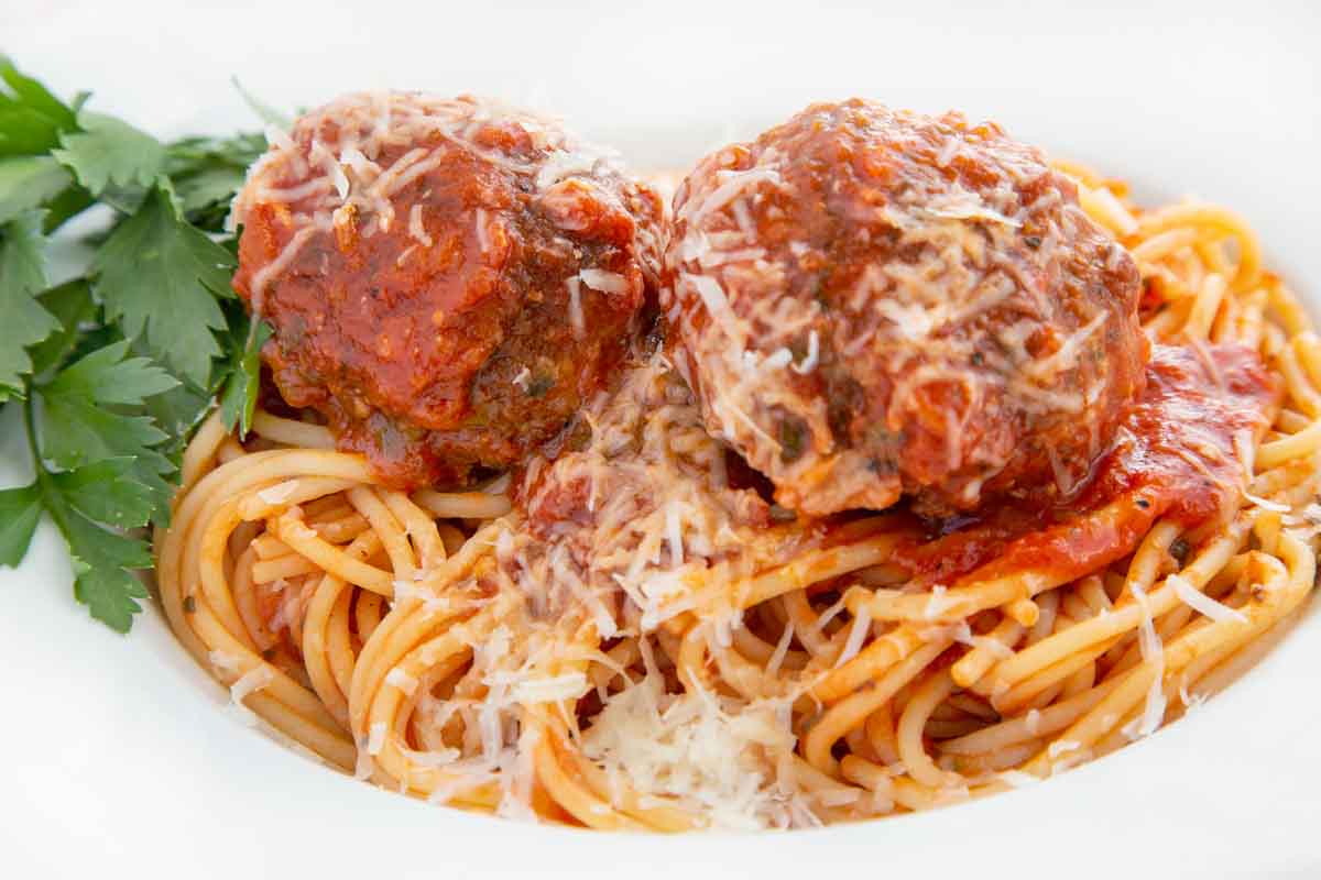 spaghetti and meatballs in a white bowl with a sprig of Italian Parsley and grated cheese