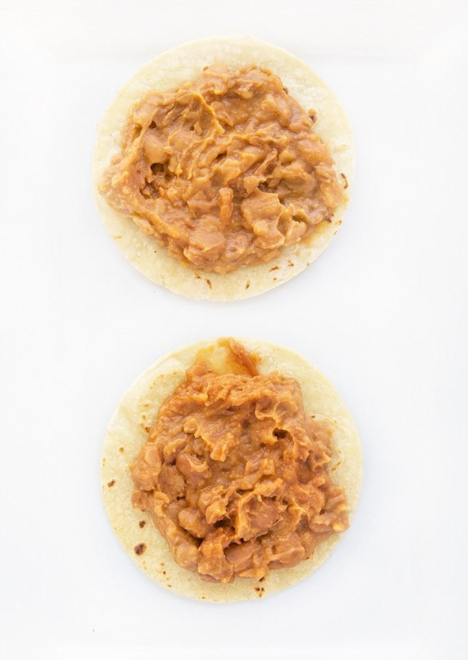 2 tortillas with refried beans sitting on a white platter.