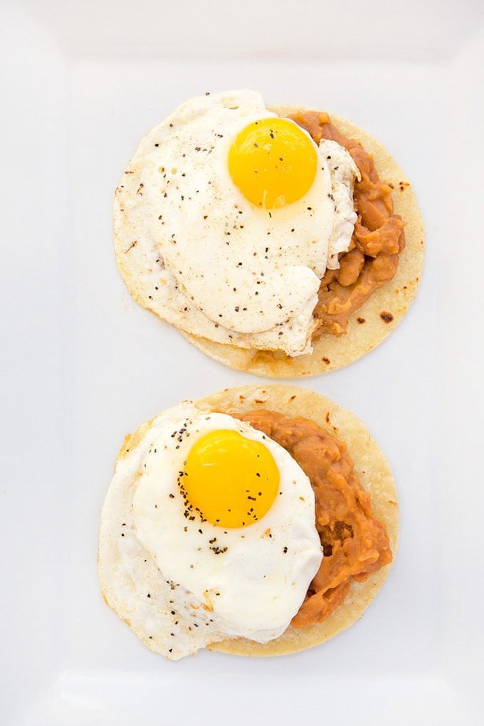 2 tortilla, beans topped with fried egg sitting on a white platter.