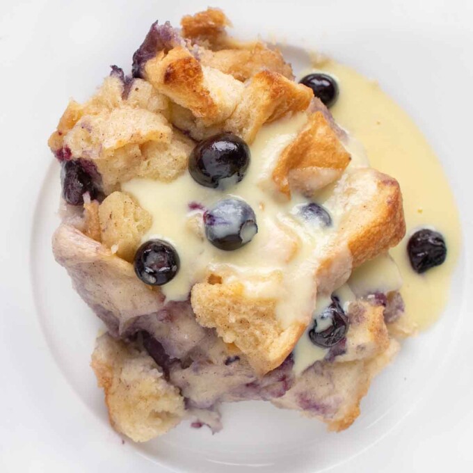 overhead shot of blueberry bread pudding on a white plate with creme anglais