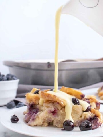 pouring creme anglais from a pitcher onto a portion of blueberry bread pudding