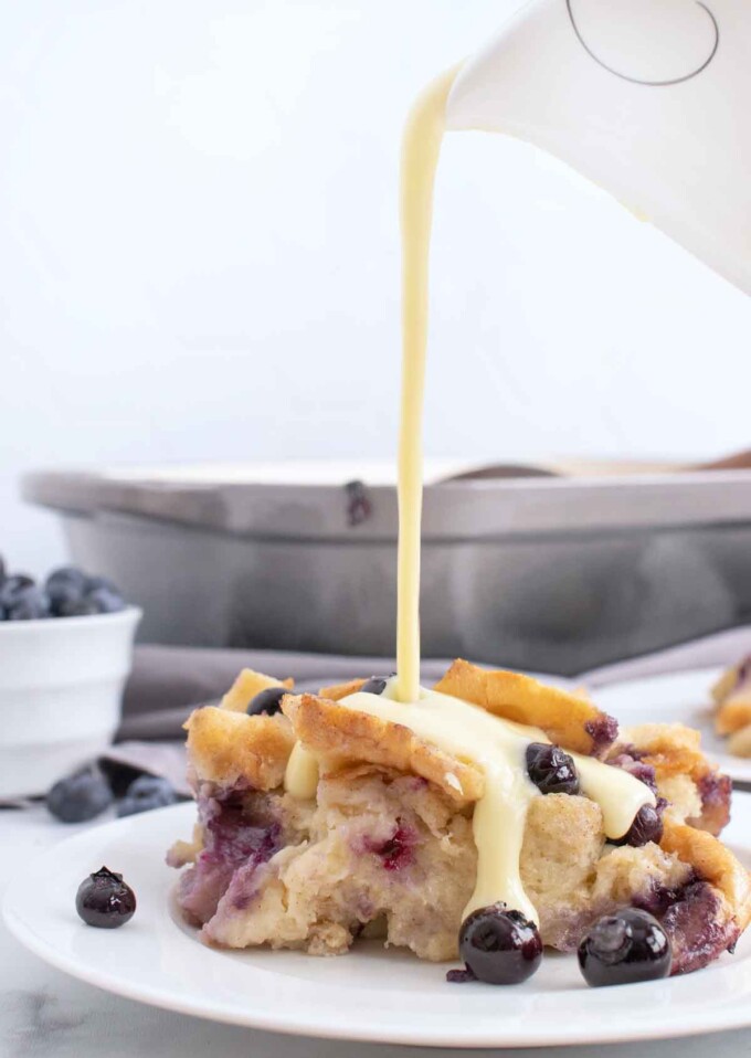 pouring creme anglais from a pitcher onto a portion of  blueberry bread pudding