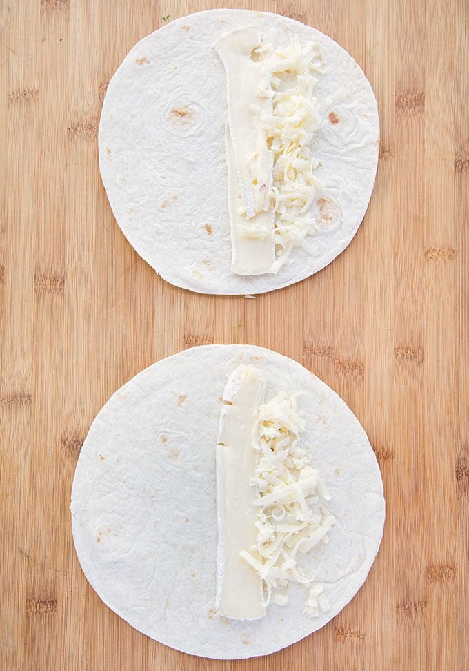 brie and shredded cheddar on two flour tortilla sitting on a wooden cutting board