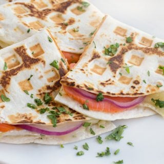 close up side view of smoked salmon quesadillas cut in half sitting on a white plate with a cilantro garnish