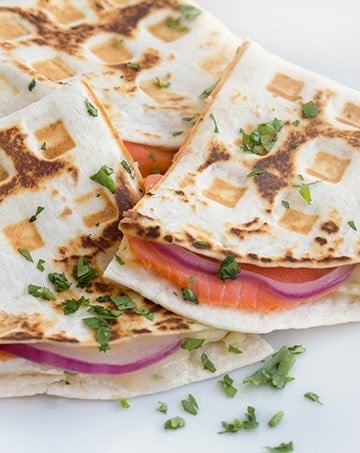 close up side view of smoked salmon quesadillas cut in half sitting on a white plate with a cilantro garnish