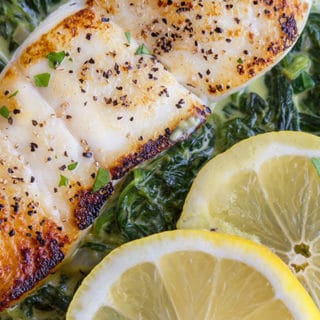 pan seared halibut on a bed of creamed spinach with a partial view of 2 lemon slices