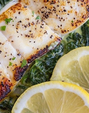 pan seared halibut on a bed of creamed spinach with a partial view of 2 lemon slices