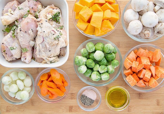 ingredients for chai marinated chicken and roasted vegetables in bowls sitting on a wooden cutting board