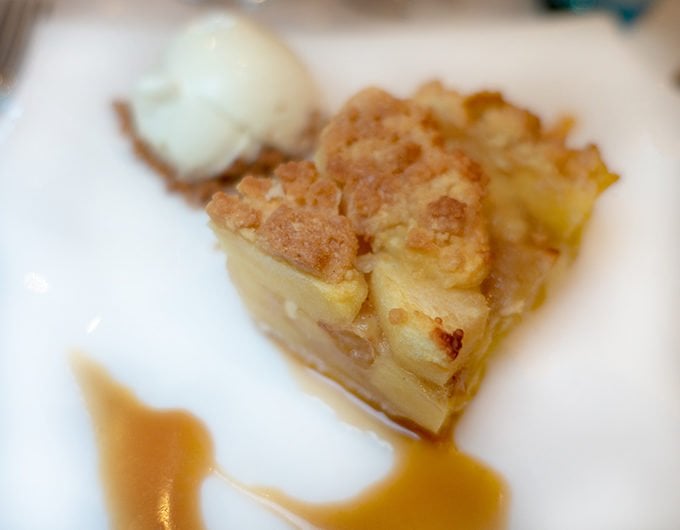 apple crumble pie with a caramel sauce and vanilla ice cream on a white plate