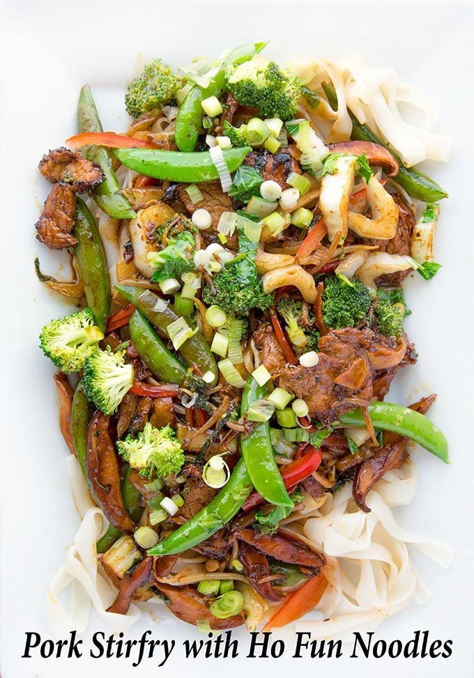 Stir Fried Pork with vegetables on a bed of Ho Fun Noodles on a white platter