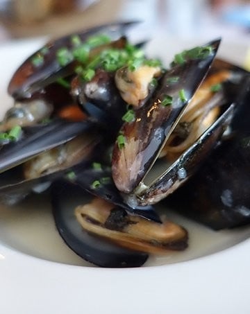 Mussels served in a white bowl sprinkled with chopped shallots