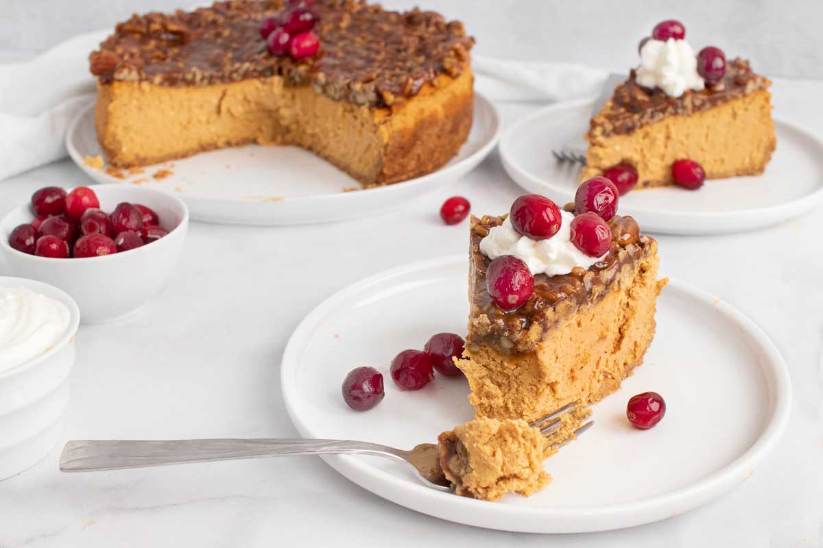 slices of pumpkin. praline cheesecake on white plates with the rest of the cheesecake in the background