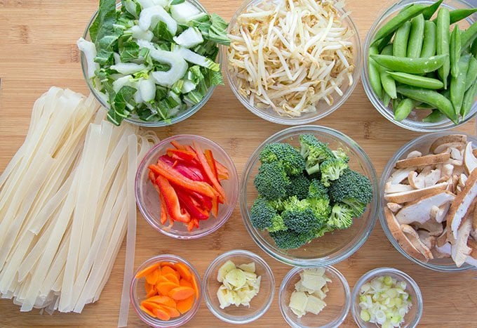 vegetables for stir fry and ho fun noodles sitting on a wooden cutting board