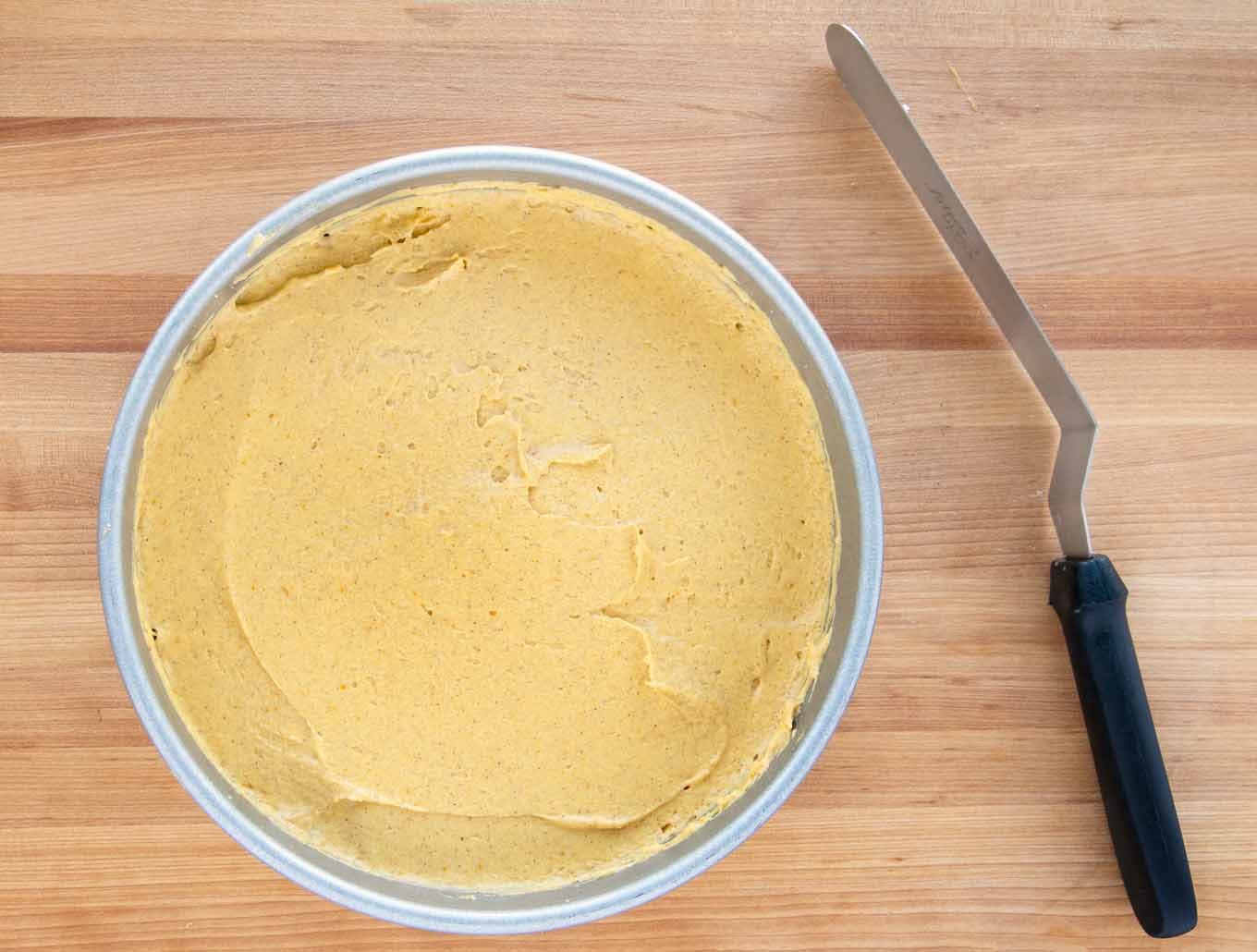 batter added to cake pan with a black handled spatula next to it