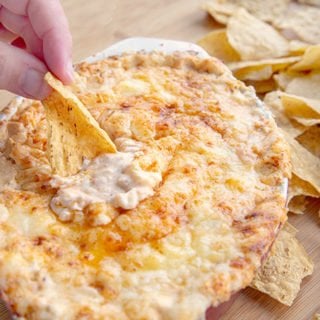 hand scooping out Cheddar lobster dip with a Mission Tortilla chip