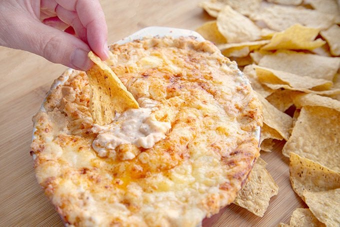 hand scooping out Cheddar lobster dip with a Mission Tortilla chip