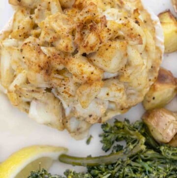 overhead shot of baked crab imperial on a white plate with sauteed greens and roasted potatoes