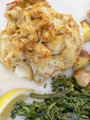 overhead shot of baked crab imperial on a white plate with sauteed greens and roasted potatoes