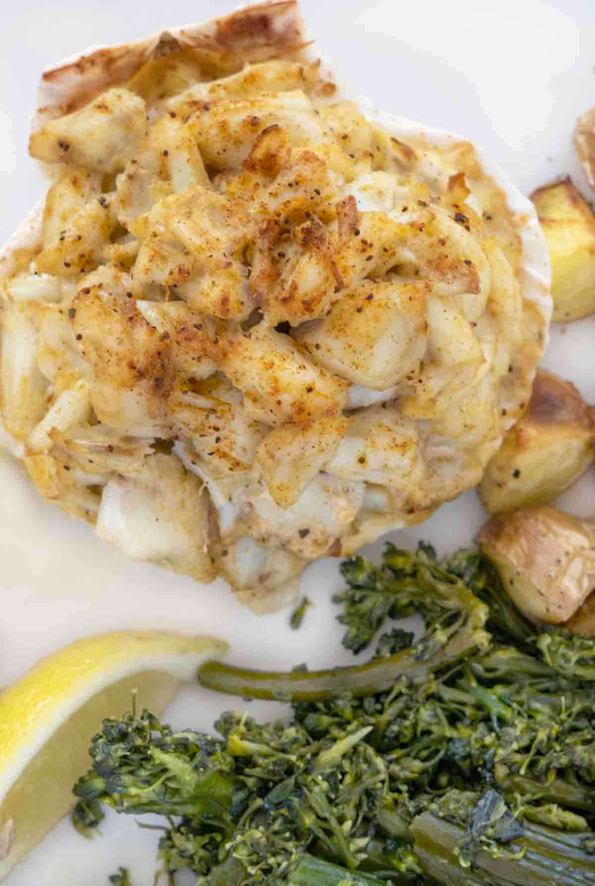 overhead shot of baked crab imperial on a white plate with sauteed greens and roasted potatoes