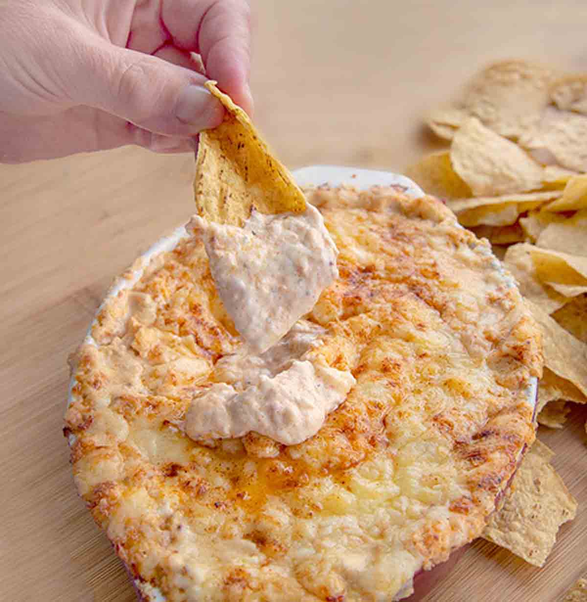 hand dipping into cheddar lobster dip with a tortilla chip