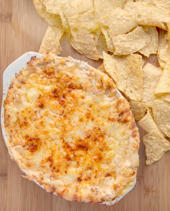 baked lobster dip next to tortilla chips on a cutting board