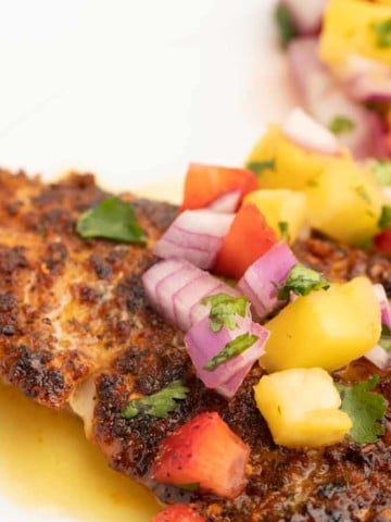 cooked cajun style florida snapper fillet with fruit salsa and lime margarita sauce on a white plate