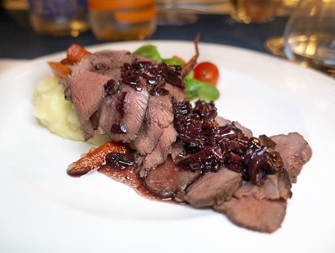 sliced duck breast with cherries on a white plate