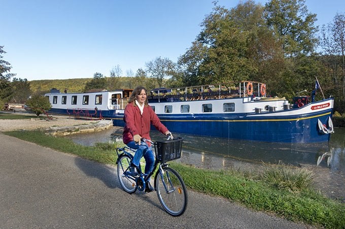 woman biking along the towpath next to a European Waterways Barge