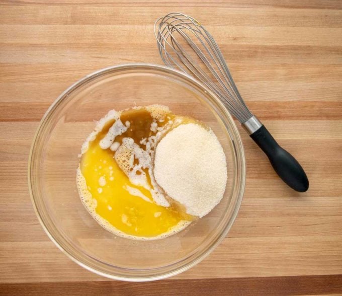melted butter, vanilla and sugar added to bowl of eggs with wire whisk next to the bowl