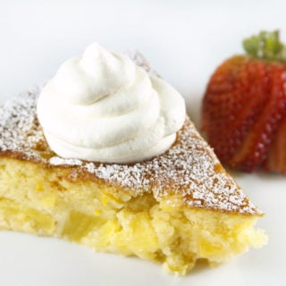 slice of pineapple butter cake with whipped cream on top and a sliced strawberry behind it