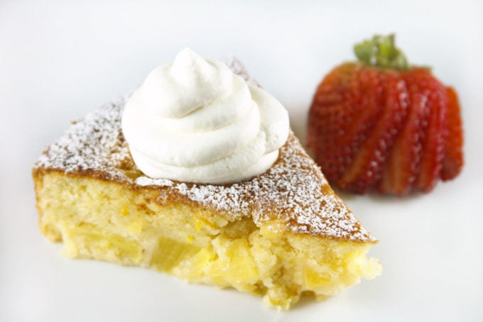 slice of pineapple butter cake with whipped cream on top and a sliced strawberry behind it