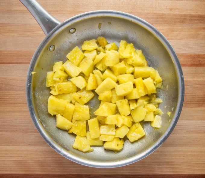 cooked pineapple chunks in saute pan on wooden cutting board