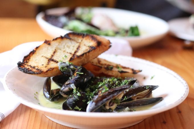 mussels with a sauce in a white bowl with grilled slices of french bread