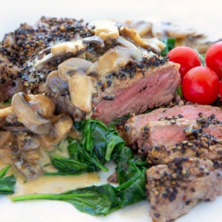steak au poivre sliced showing medium rare steak served with wilted spinach and cherry tomatoes