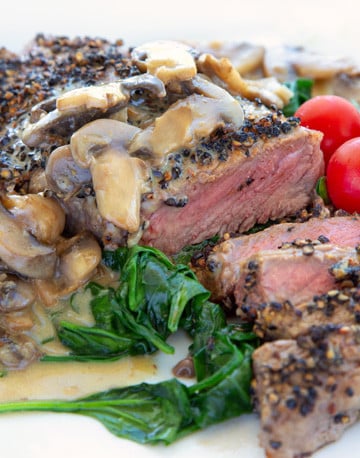 steak au poivre sliced showing medium rare steak served with wilted spinach and cherry tomatoes