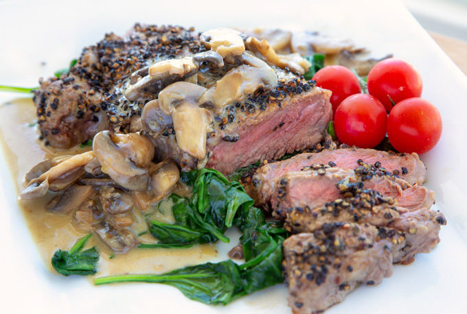 steak au poivre sliced showing medium rare steak served with wilted spinach and cherry tomatoes