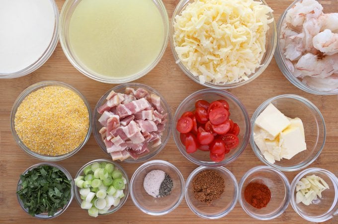 ingredients to make cheesy grits and shrimp in glass bowls on wooden cutting board