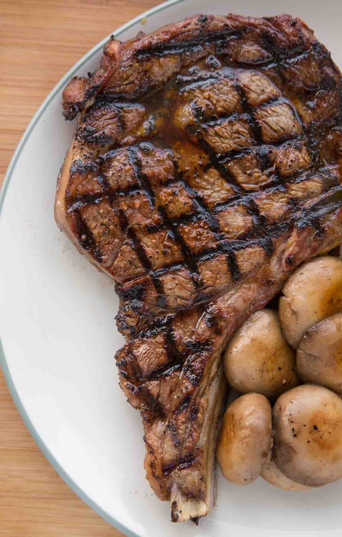 crosshatch marked ribeye steak on white plate with grilled mushrooms
