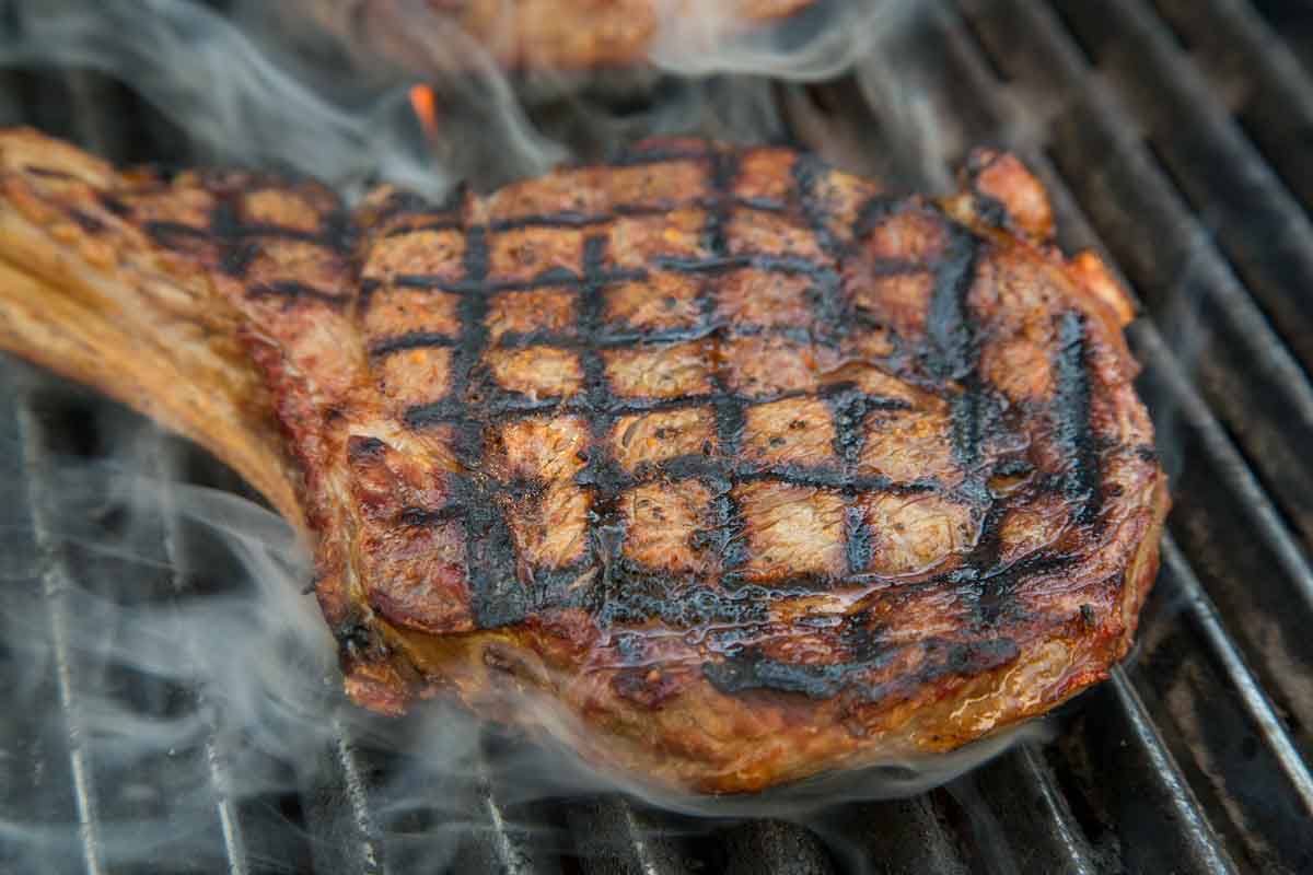 Ribeye with crosshatch marks on the grill with smoke coming off of it